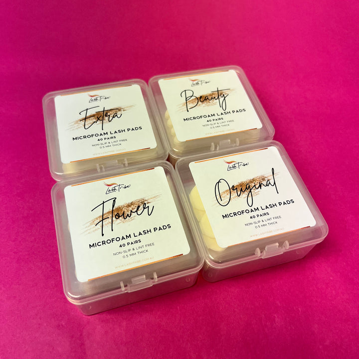 Four Microfoam Eye Pads in plastic containers on a pink background, by Lash Tribe.