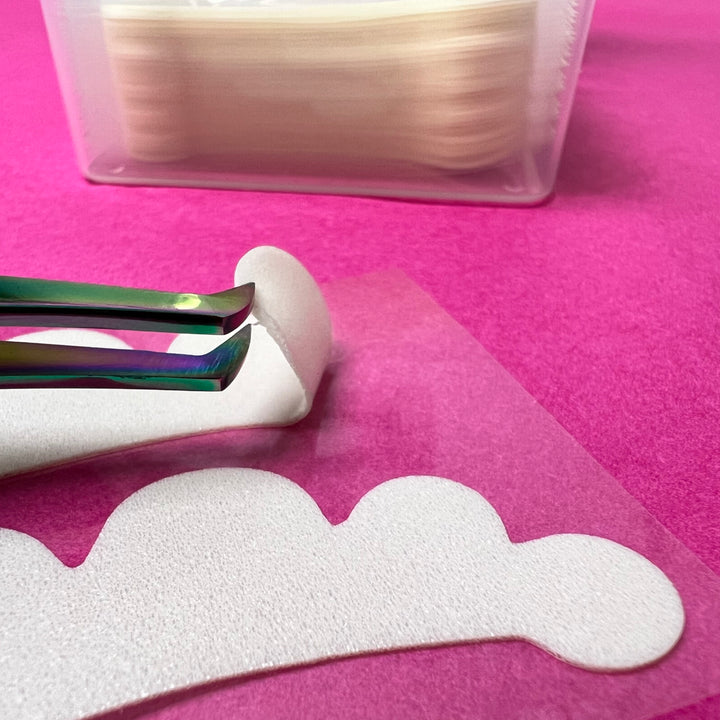 A pair of Lash Tribe Microfoam Eye Pads is being used to cut a piece of paper.