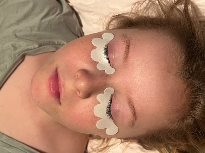 A woman laying on her bed with a pair of Lash Tribe Microfoam Eye Pads.