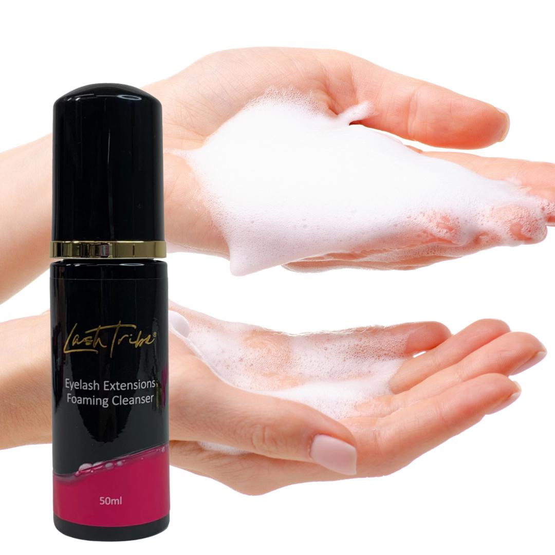 A woman's hand holding a bottle of Lash Tribe Eyelash Extensions Foaming Cleanser for her eyelash extensions.