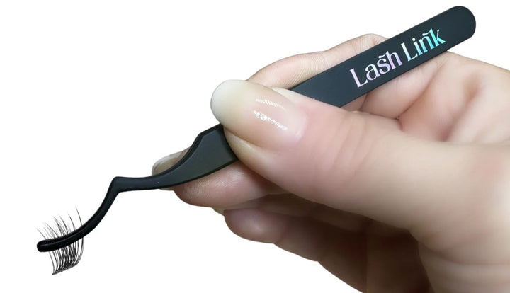 A hand holds the elegant Lash Link Applicator | Lash Segment Tweezer by Lash Link, a black tool resembling tweezers, delicately poised with a small set of false eyelashes on its tip.