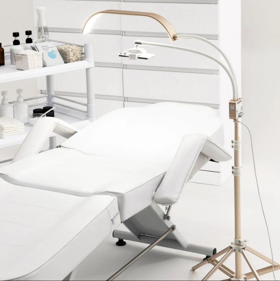 A white bed with the Lash Tribe GLAMCOR Horizon Pro Kit | Light for Lashing in the middle, providing lighting for a lash artist.