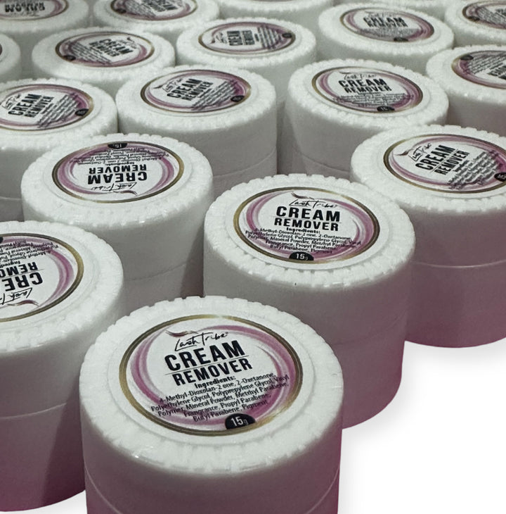 Several white containers labeled "Lash Tribe® Cream Remover" are arranged in rows. Each container, designed for professional use, has a circular white cap with a product label featuring pink and black text. This quick and gentle eyelash extensions remover ensures efficient service without compromising care.