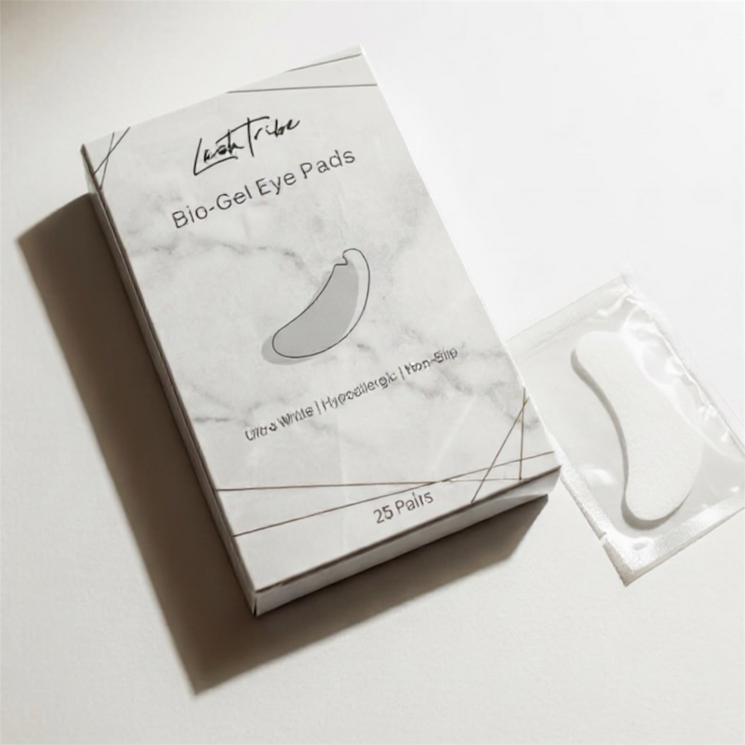 A box labeled "NEW Under Eye BIO Gel Pads" by Lash Tribe with a minimalist design sits beside a sealed eye pad, perfect for eyelash extensions and safe for sensitive skin, displayed on a flat surface under soft lighting.