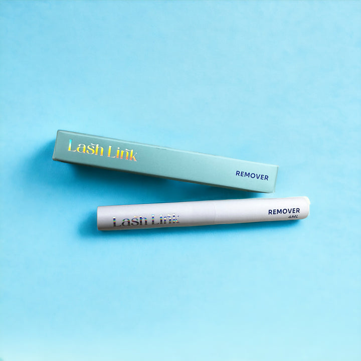 A white tube labeled "Lash Link Extension Remover Oil" and a teal box on a light blue background offer a refreshing lash solution. Ideal for DIY enthusiasts looking for an effective eyelash extension remover from Lash Link.