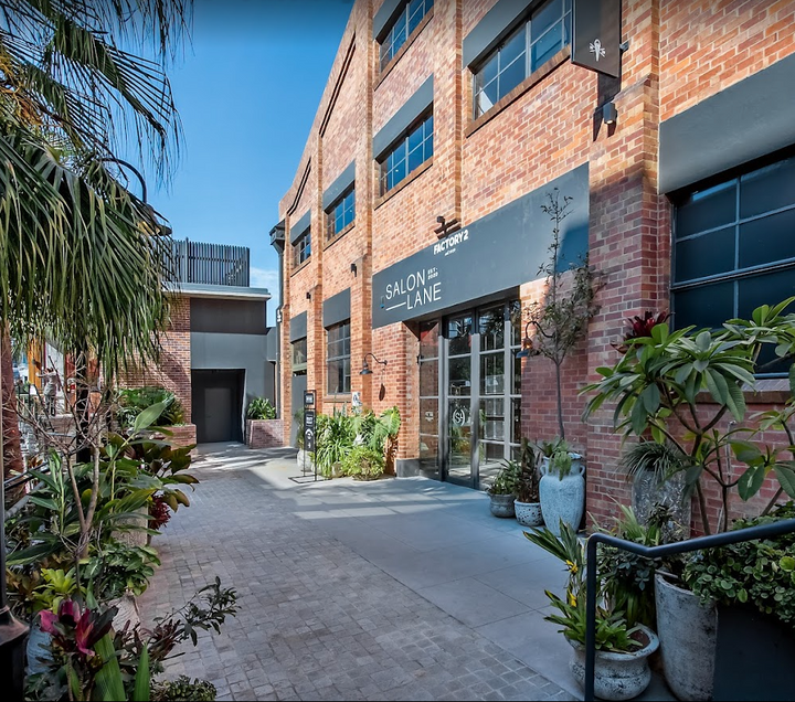 The entrance to a brick building with potted plants features the SALON SOCIAL EVENT | October 7th by Lash Tribe.