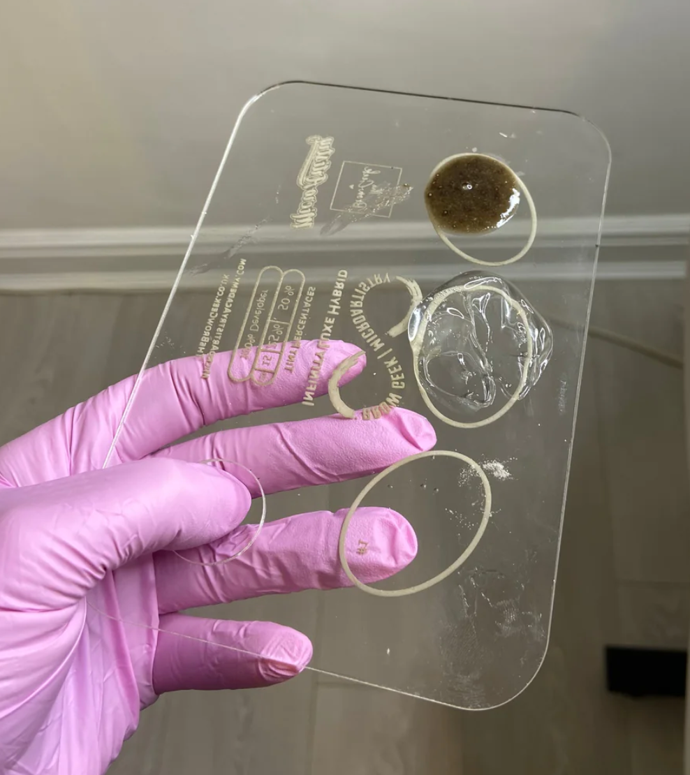 a person holding up a clear plastic INFINITY LIFT & TINT PALETTE by Lash Tribe, which is used for eyebrow and lash lifting.