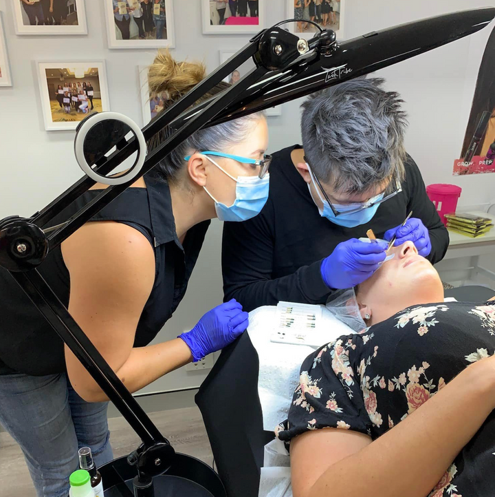A woman is getting her eyebrows done with the Beginners Eyelash Extension Training | 3 Day Lash Course by Lash Tribe in a salon.