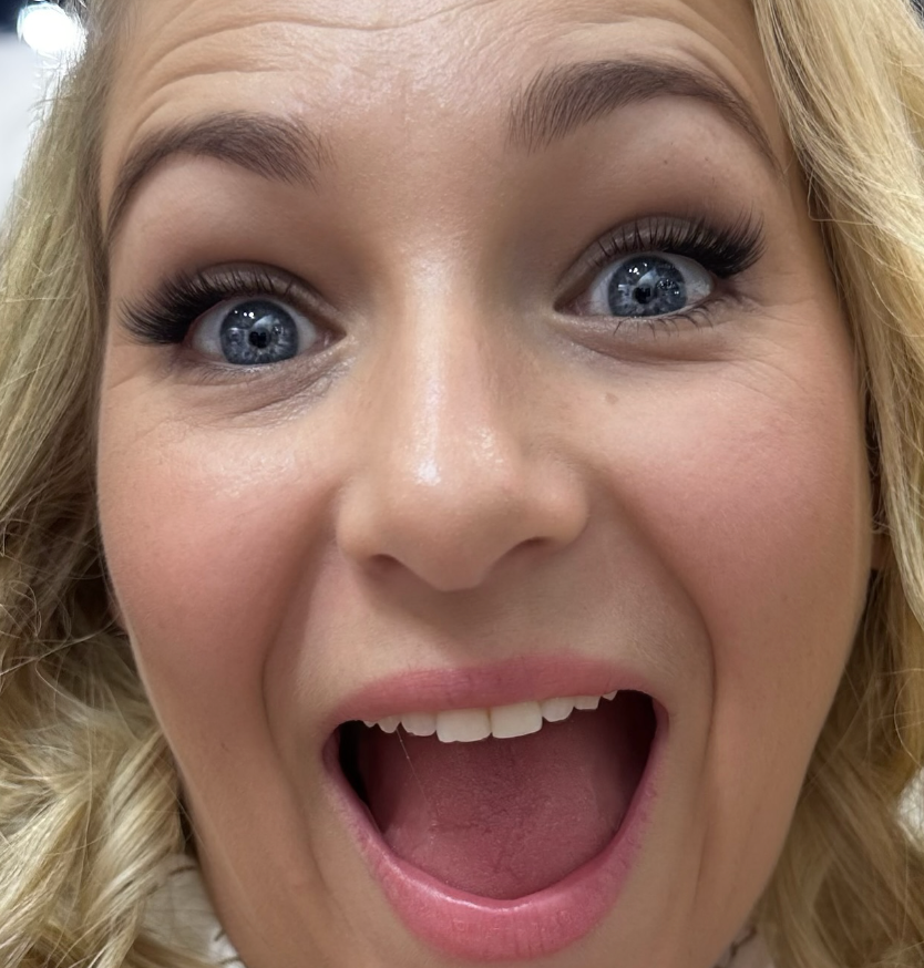 A person with blue eyes and blonde hair is smiling widely, showcasing their expertly applied makeup and Lash Link DIY Eyelash Extension Kit.