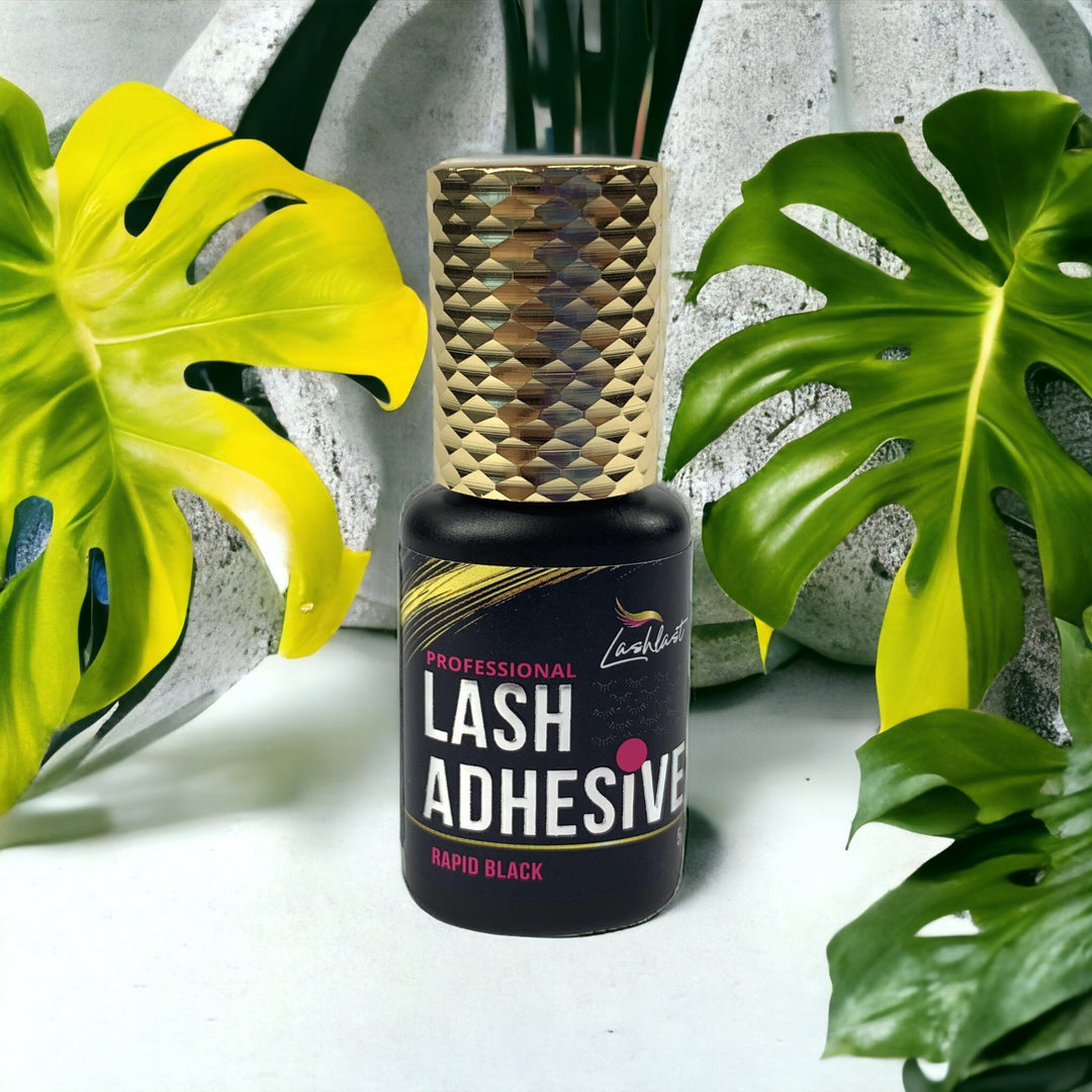 a bottle of Lash Tribe Rapid Black Adhesive in front of a tropical plant.