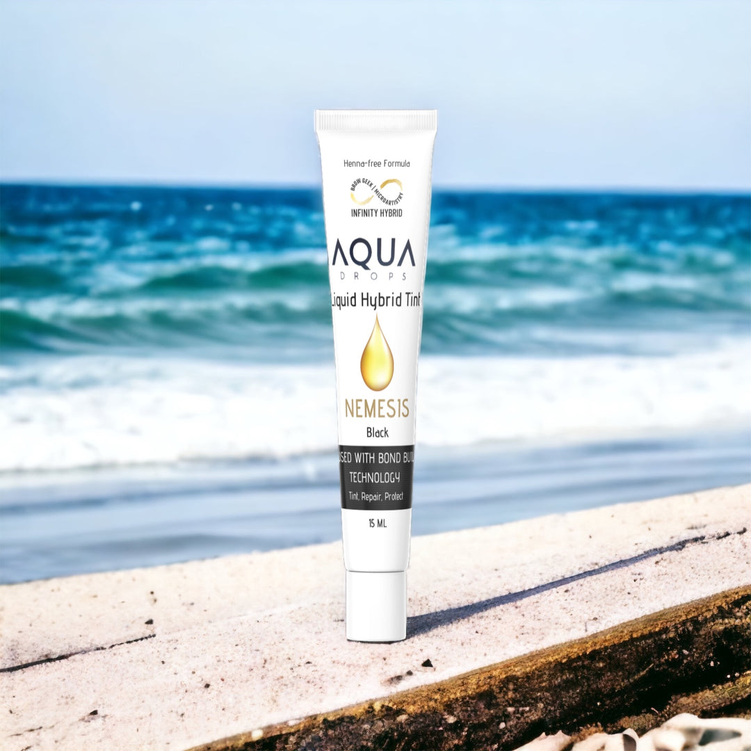 A tube of Infinity Aqua Drops | Hybrid Brow Tint Single Tubes by Lash Tribe on a beach in front of the ocean.