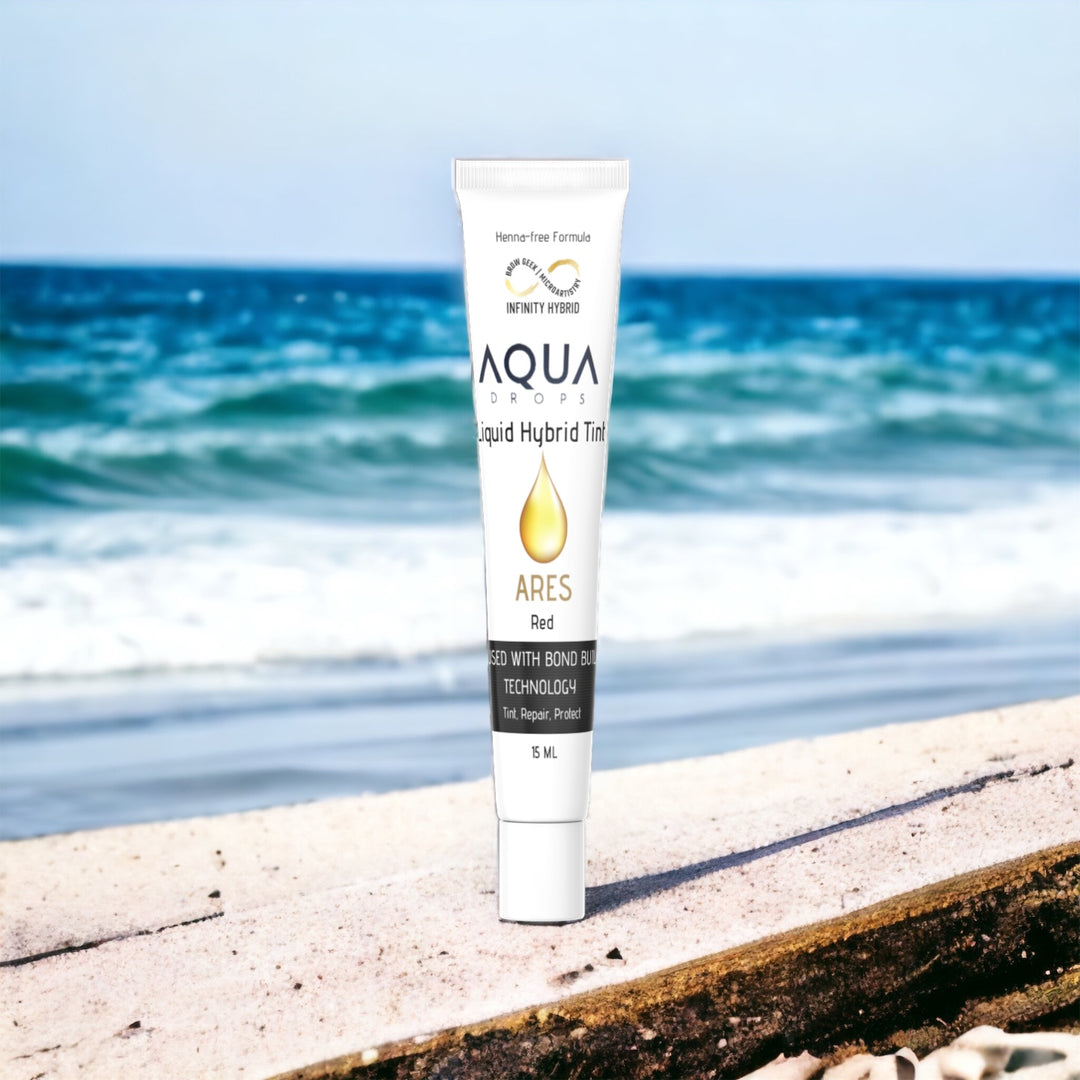 A tube of Infinity Aqua Drops facial oil sitting on a beach.