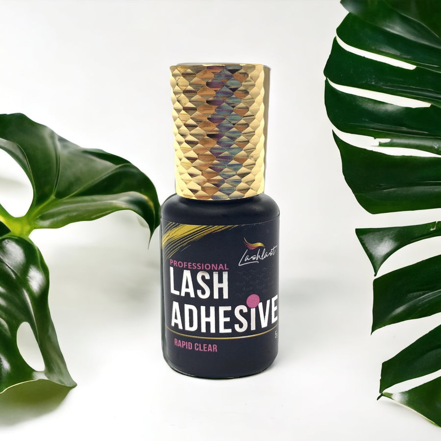 A bottle of Lash Tribe Rapid Clear Adhesive, a clear lash glue for eyelash extensions, next to a green leaf.