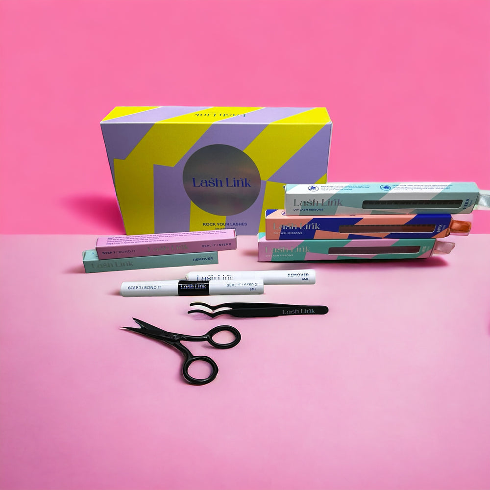 On a pink background, the Lash Link DIY Eyelash Extension Kit showcases scissors, tweezers, and assorted pastel-colored labeled product boxes and tubes, ideal for trying different lash styles.