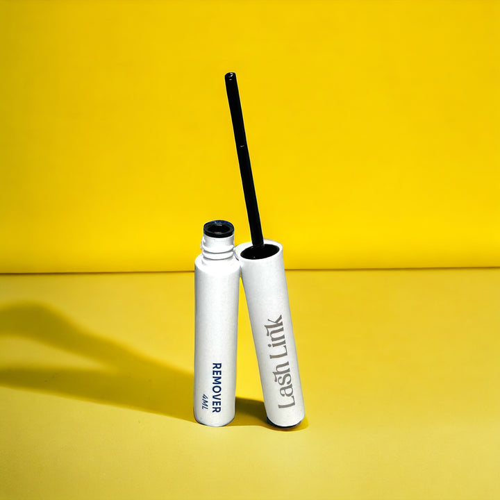 Against a vibrant yellow backdrop, the Lash Link Remover Extension Oil stands with its open black cap, perfect for a DIY lash refresh.