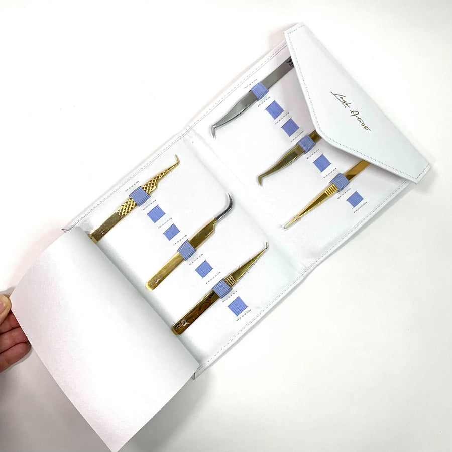 A person is holding a Lash Tribe Tweezer Envelope with a set of gold tweezers.