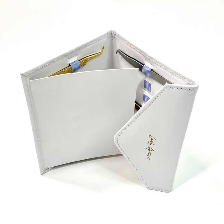 a white Lash Tribe leather wallet with a pair of Tweezer Envelope glasses and a pen.