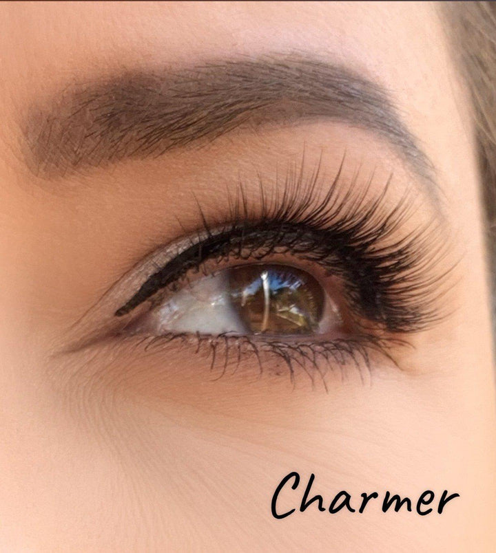 A close up of a woman's eye with Silk Magnetic Lashes by Lash Tribe and the word charmer.
