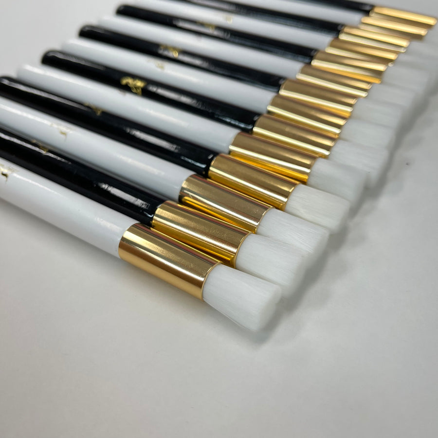 a row of white and gold Lash Tribe Cleansing Brushes for Eyelash Extensions on a white surface.