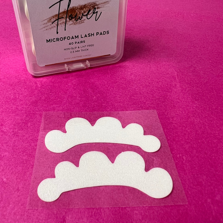 A pair of Microfoam Eye Pads by Lash Tribe, shaped like white clouds, on a pink background.
