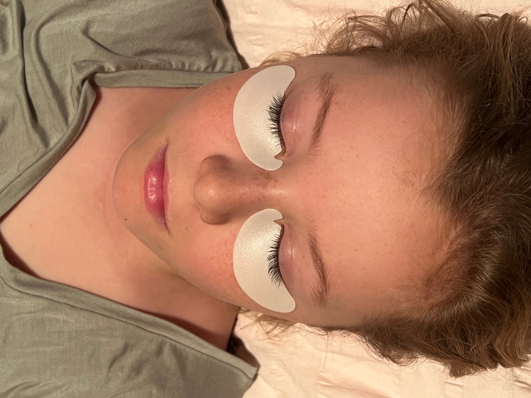 A woman laying in bed with a pair of Lash Tribe Microfoam Eye Pads.