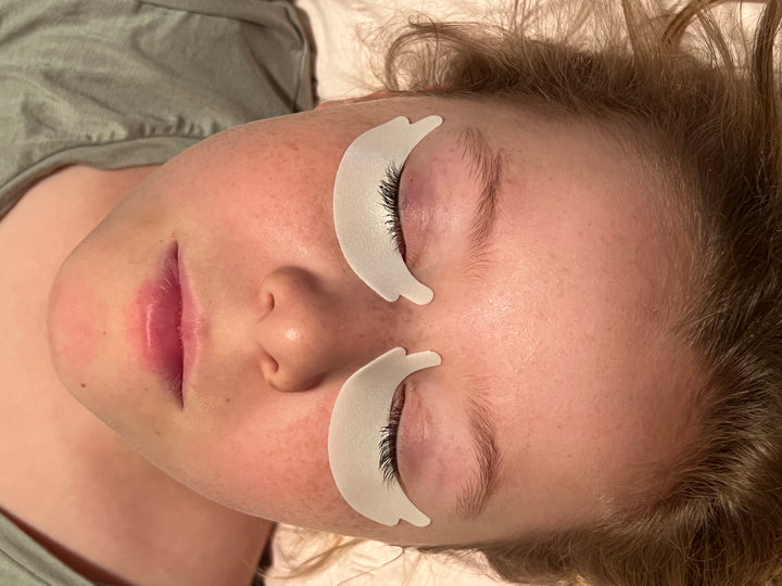 A girl laying on her bed with a pair of Lash Tribe Microfoam Eye Pads.