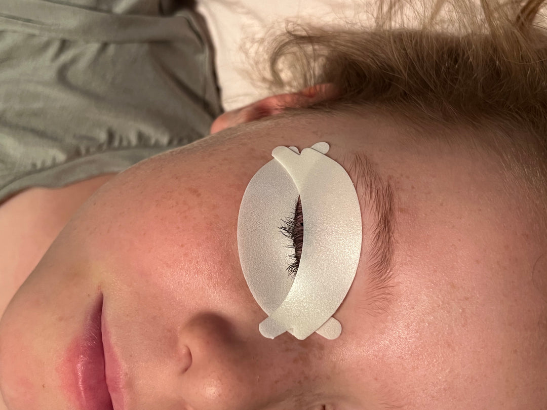 A woman laying on her bed with a pair of Lash Tribe Microfoam Eye Pads.