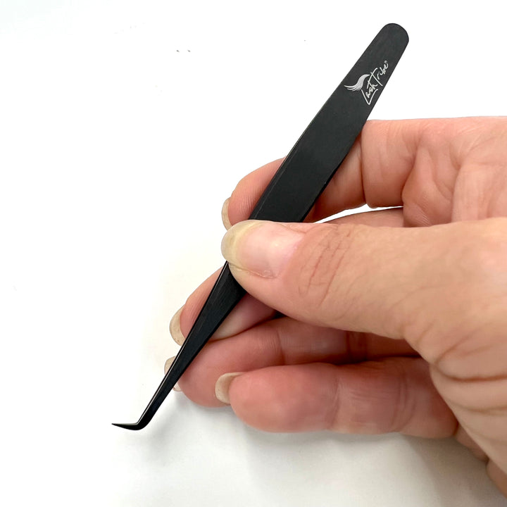 a person holding a black Nano Fibre Tip | Volume Tweezer - Black Beauty 2 by Lash Tribe on a white surface.