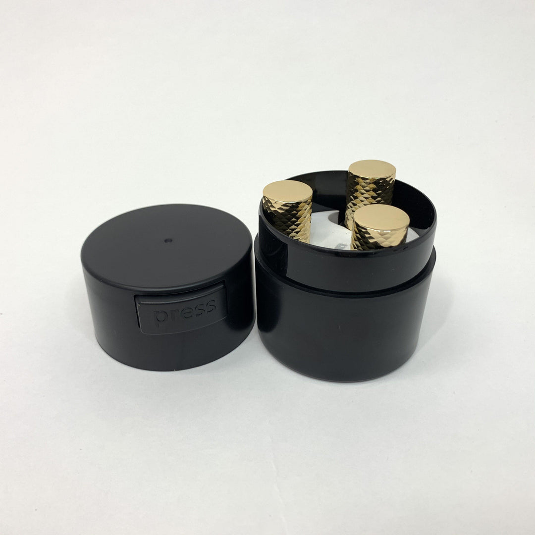 a black Lash Tribe container with two gold knobs on it.