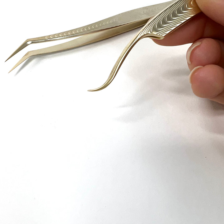 A person holding a pair of Classic Duo - Lash Tweezers from Lash Tribe on a white surface.