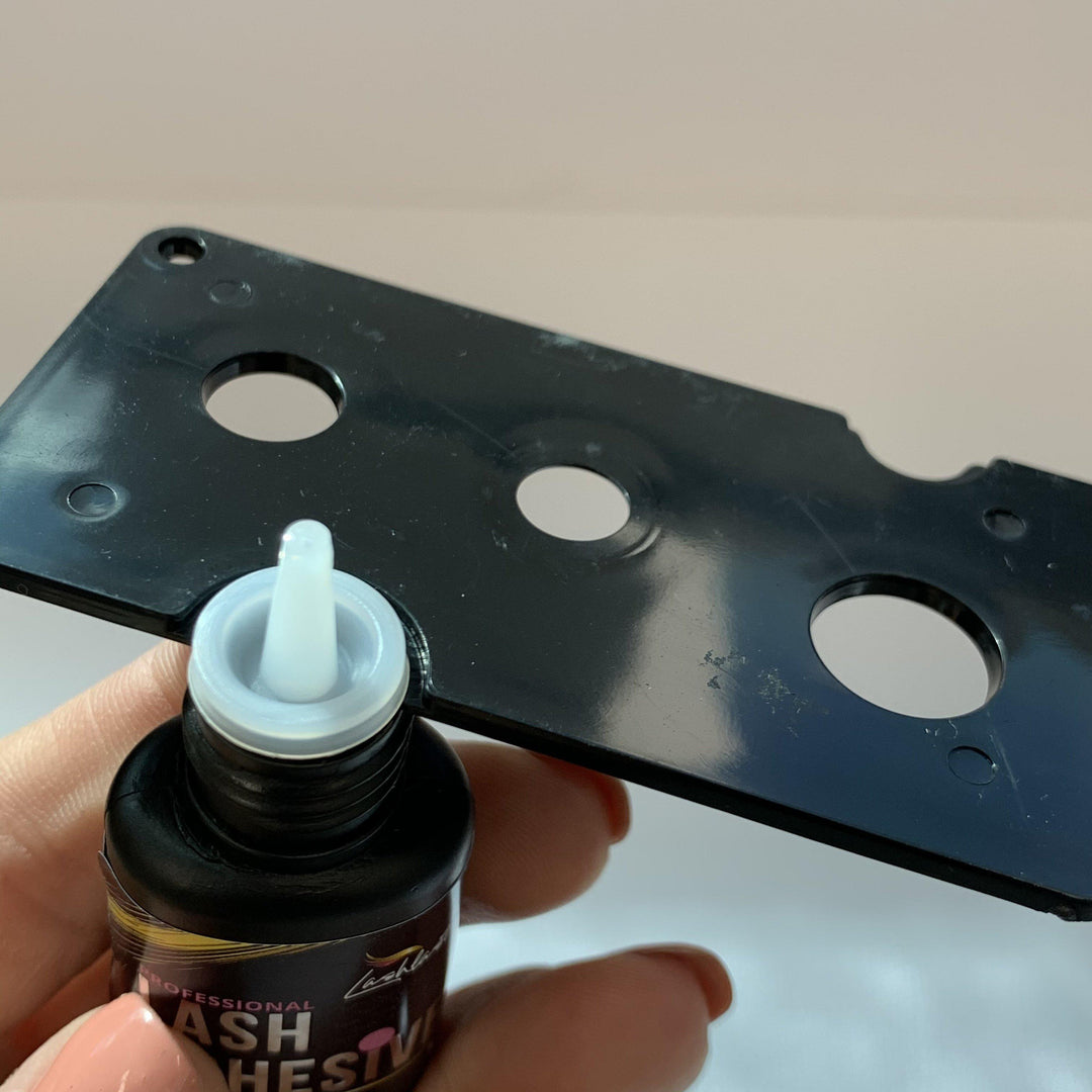 A person is using a Lash Tribe Lash Glue Nozzle Opener to unstick a bottle of glue with a stuck nozzle.