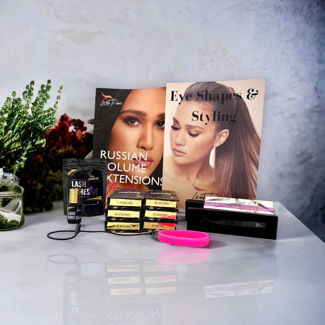 Eyelash extension products displayed on a table including boxes of lashes from the Lash Tribe Volume Eyelash Extension Starter Kit, an instruction booklet, and accessories with a decorative plant nearby.