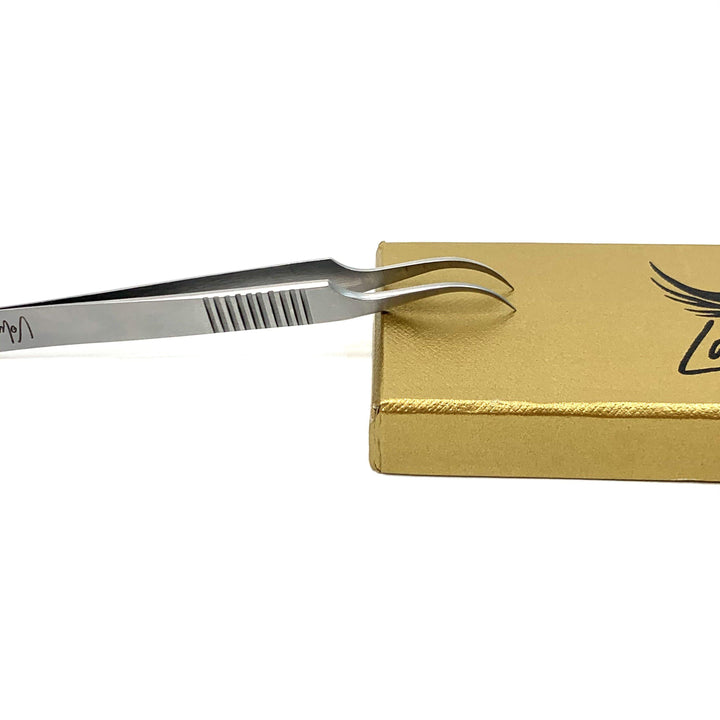a pair of Lash Tribe Volume Master | Curved Precision Tweezers on top of a gold box.