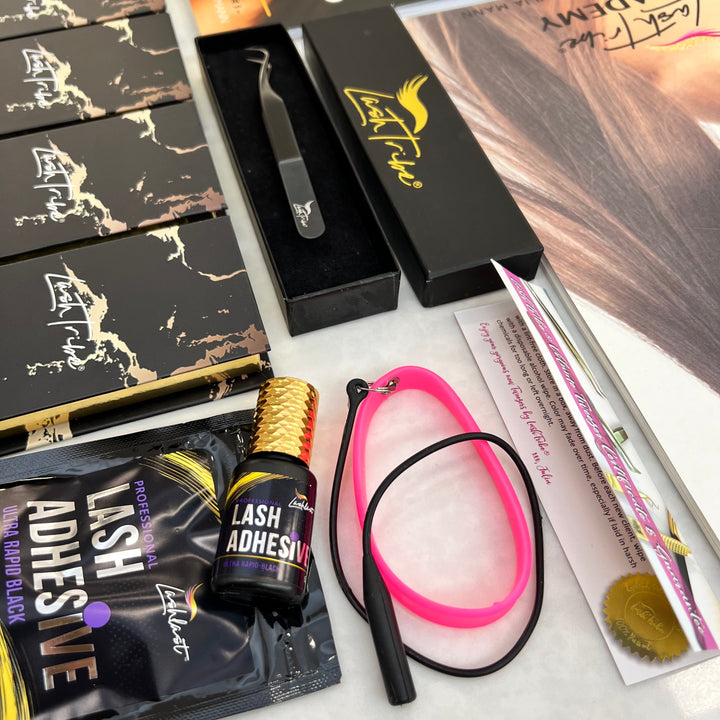 Eyelash extension supplies including boxes, tweezers in a case, Lash Tribe Volume Eyelash Extension Starter Kit, and an eyelash brush on a light surface.