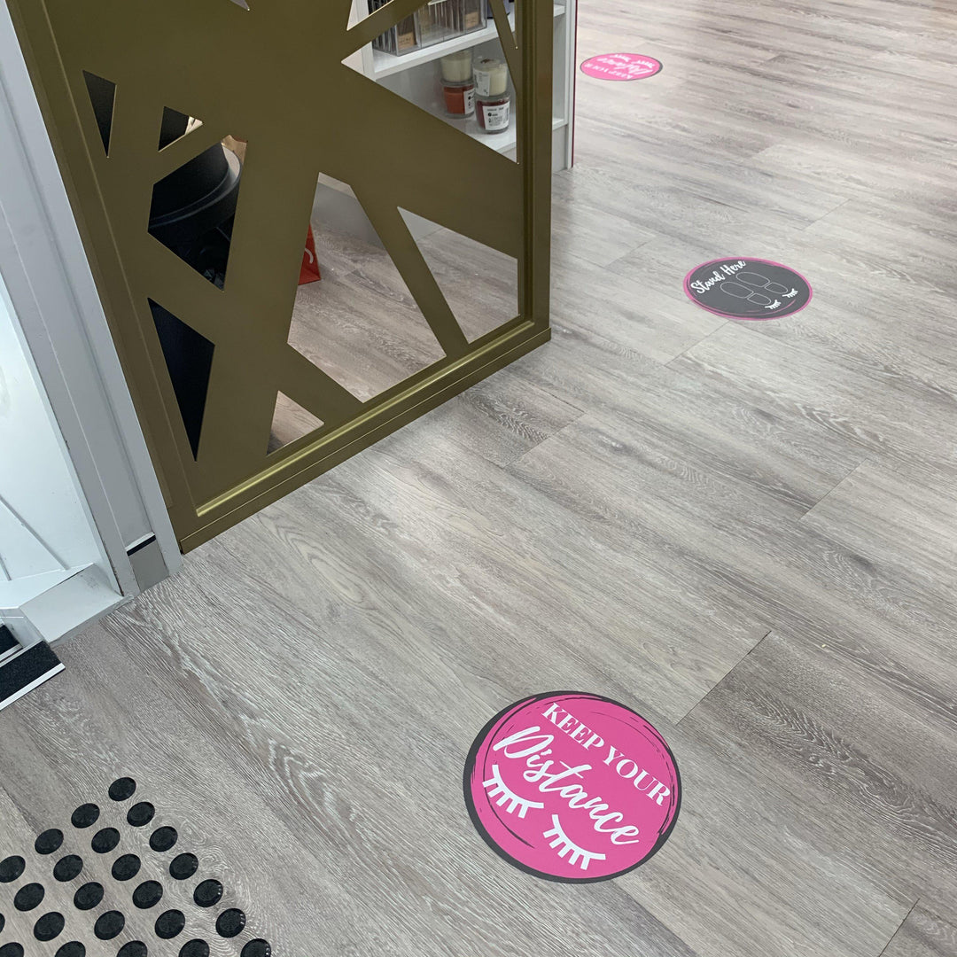 The floor of a store is decorated with pink and black Lash Tribe Social Distancing Floor Stickers.