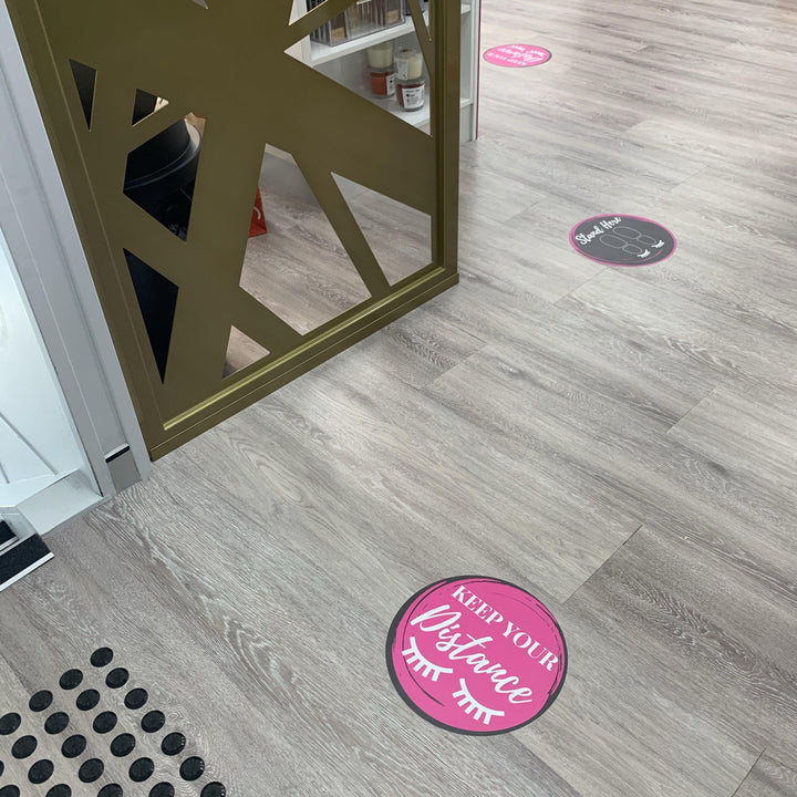 The floor of a store is decorated with pink and black Lash Tribe Social Distancing Floor Stickers.